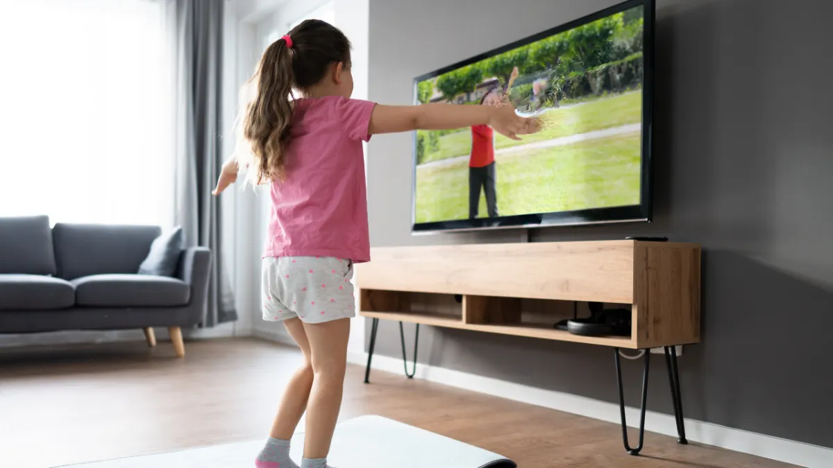 Girl stretches to the side while watching teacher on large screen TV