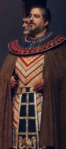 James Nathanel Salazar stands backstage, adjusting his bow tie in front of a large mirror. The room is filled with costumes and warm, golden lighting. His focused expression and elegant attire capture the anticipation before a major performance.