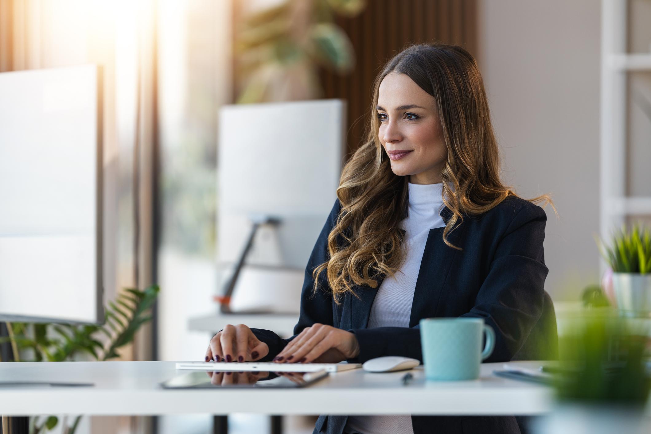 Professional woman seated at a table in natural light, wearing neutral business attire and looking confidently at the camera. She represents a fractional HR and executive leadership advisor focused on helping growing companies scale with clarity and alignment.