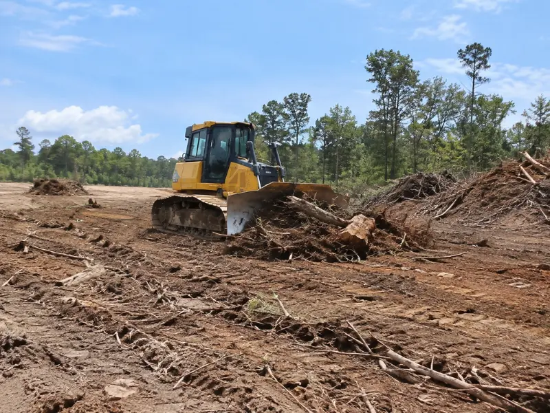 Bulldozer pushing tree stumps and roots to clear and grade a lot during land clearing services.