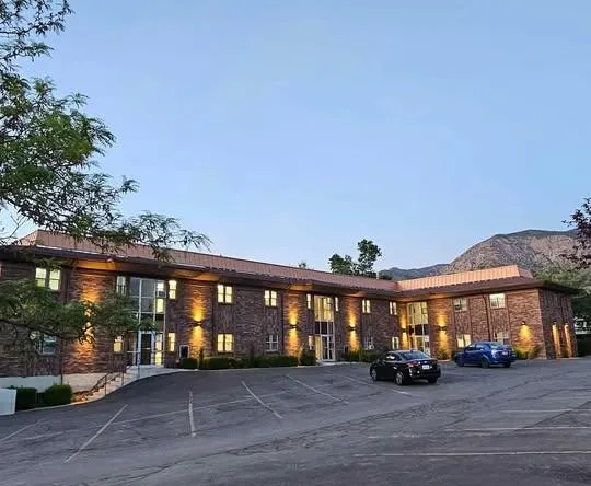 Exterior of Quincy Salon Suites in Ogden, Utah, with modern black and gold signage, large windows, and a bustling street scene with diverse people passing by. The building is surrounded by trees and city lights, exuding a welcoming, upscale vibe.