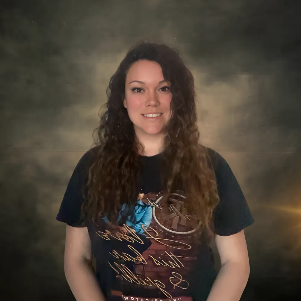 Portrait of Cheyenne Stanley, Owner of RebelRoots Creative Solutions LLC, also known as RebelRoots Marketing, smiling confidently with long curly hair and wearing a graphic t-shirt, against a textured dark background, symbolizing approachable yet professional marketing expertise.