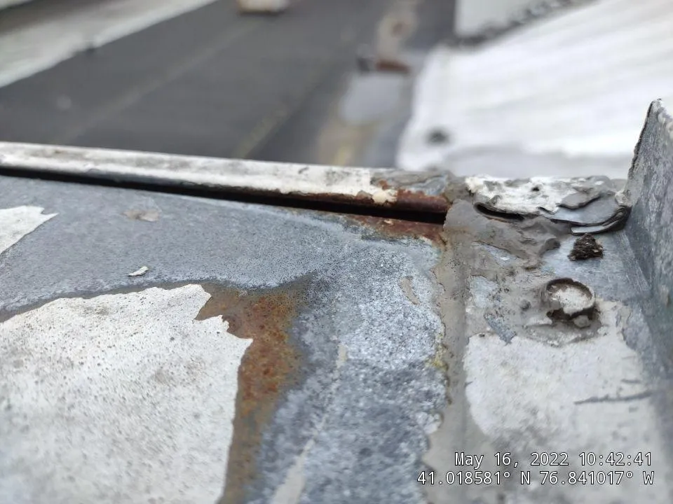 Close-up view of a deteriorating flat roof showing significant rust damage, peeling coatings, and metal corrosion around roof penetrations and seams. - Schultz Roofing, Inc