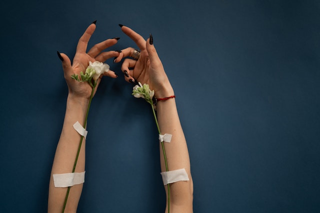 a hands with black nails and white flowers showing IV