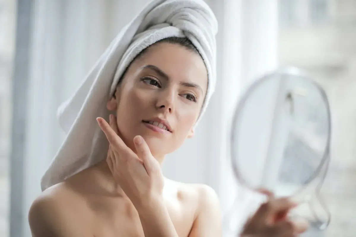 a person with a towel on her head looking at a mirror to imrove skin