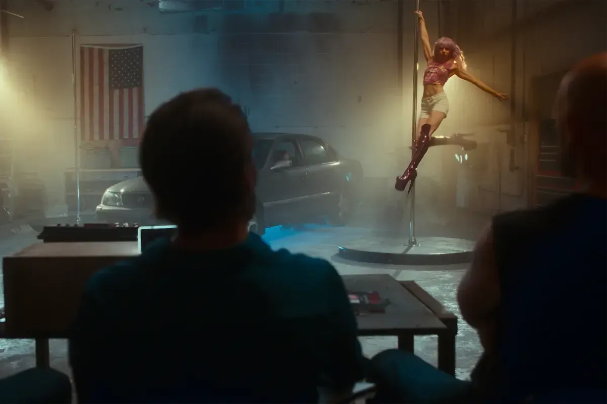 People sitting at table watching woman dance on stripper pole next to car