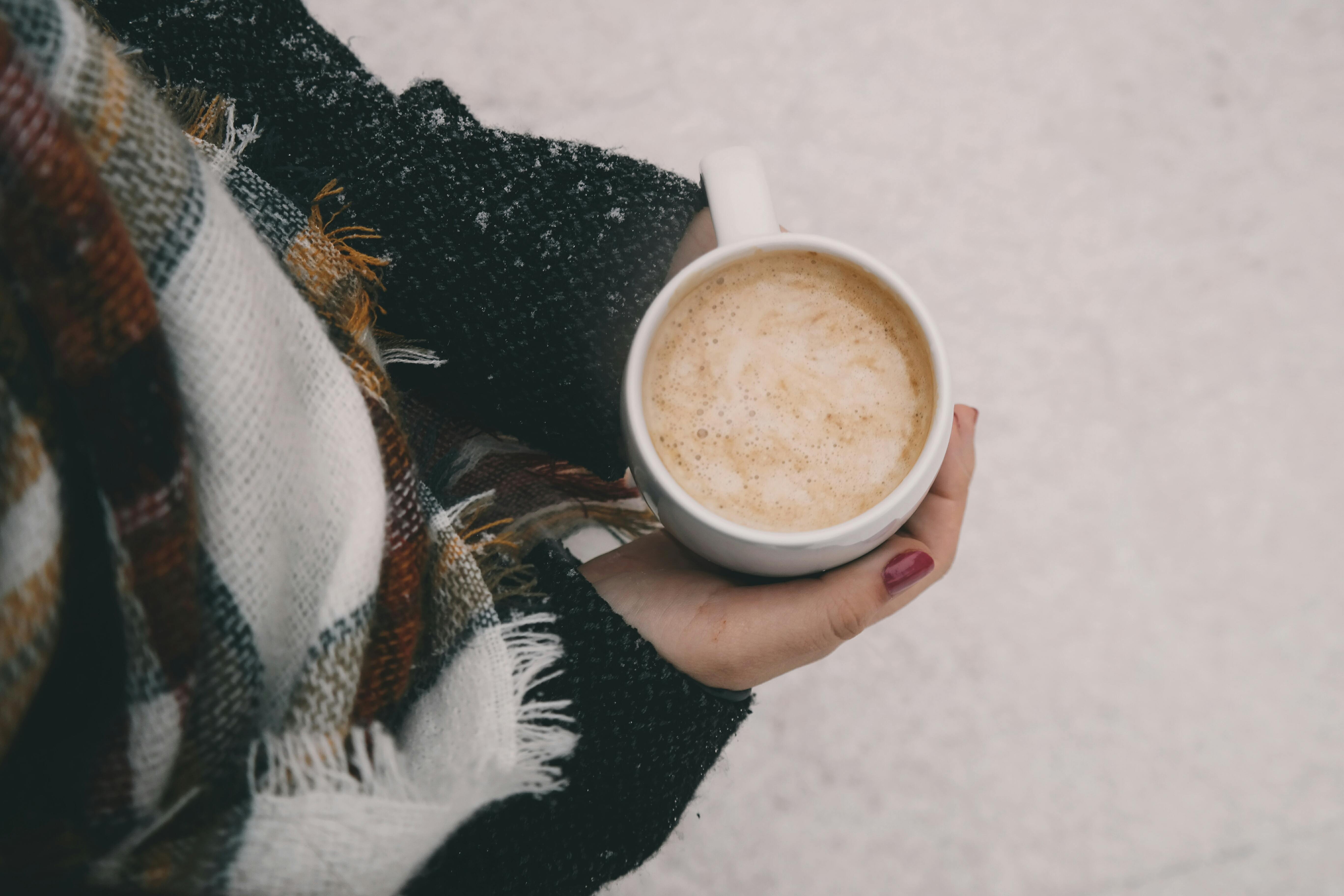Person holding a warm drink outdoors in cold weather, contrasting indoor comfort with the need to protect plumbing during Memphis winter freezes.