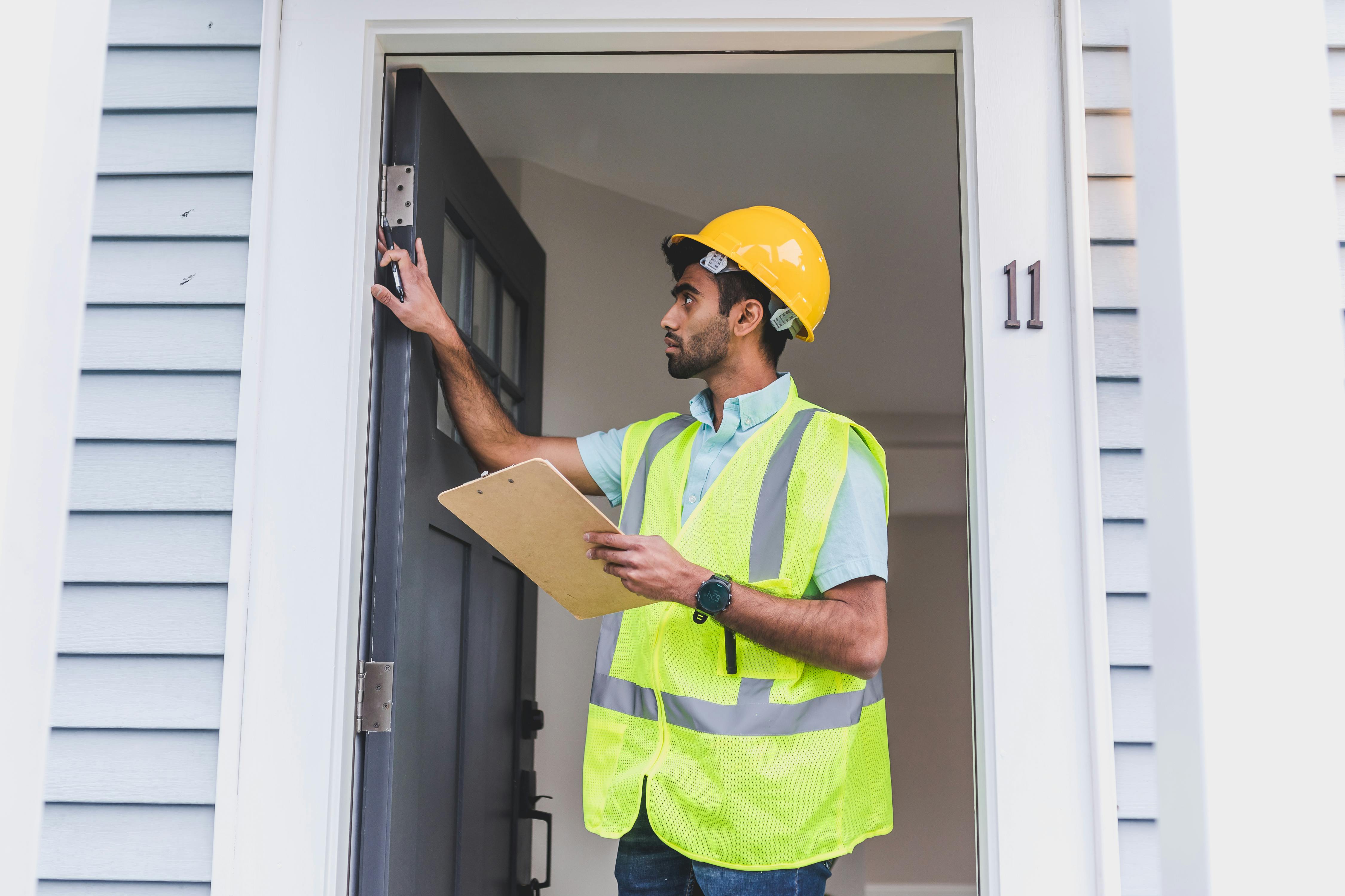 Home inspector checking an entry door in a Memphis house while reviewing a checklist, a common step before listing a home for sale.