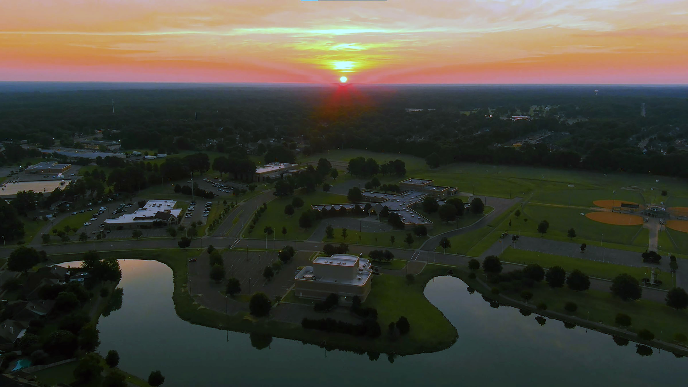 Aerial sunset view over Bartlett, Tennessee showing mature neighborhoods, community buildings, and tree-lined streets typical of older Mid-South homes.