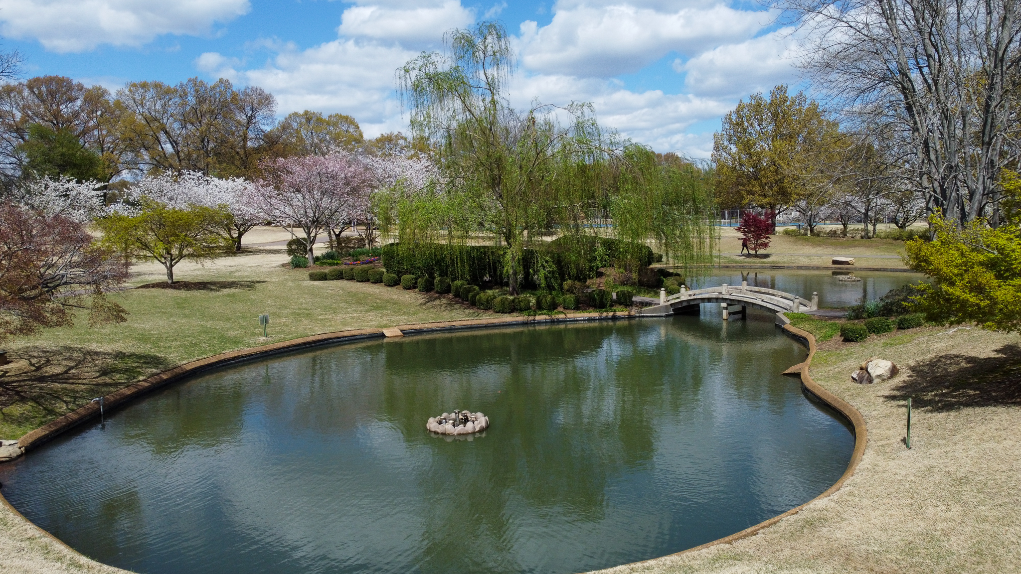 Neighborhood park in Bartlett, Tennessee with a pond, footbridge, and mature trees surrounded by long-established residential areas.