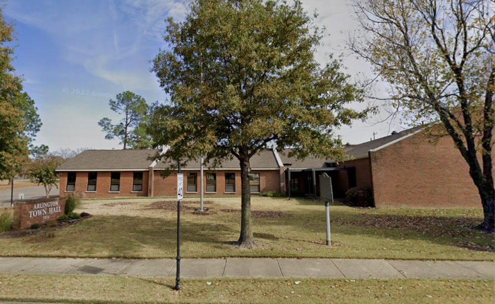 : Arlington Town Hall building in Arlington, Tennessee with brick construction, mature trees, sidewalks, and surrounding civic grounds.