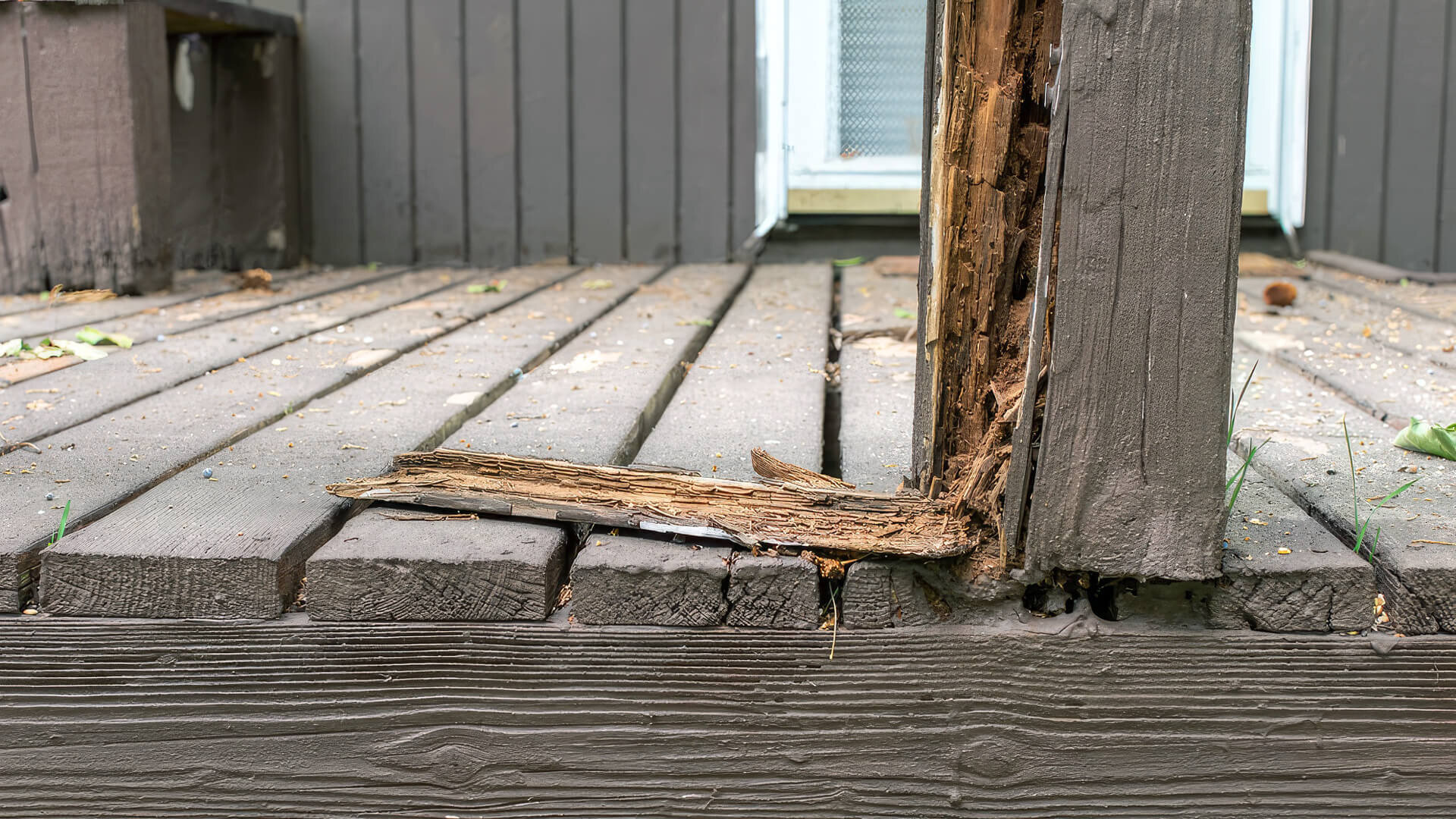 Close-up of a rotted wooden deck post and deteriorated deck boards showing moisture damage and structural decay.
