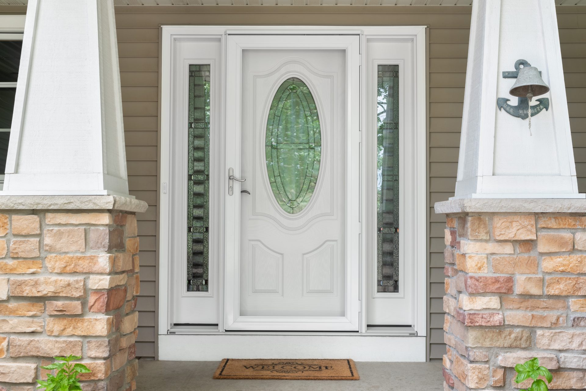 White front entry door with decorative glass and sidelights installed on a residential home with stone columns and vinyl siding.