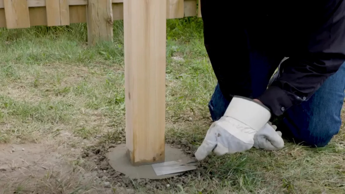 Wooden fence post set in fresh concrete footing at ground level during fence installation.