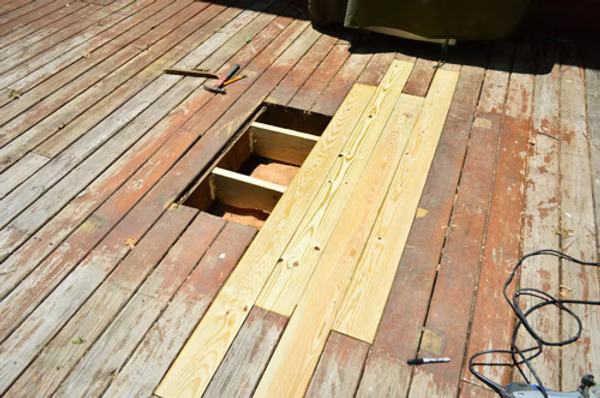 Damaged wooden deck with a section removed and new pressure-treated boards being installed during a deck repair project.