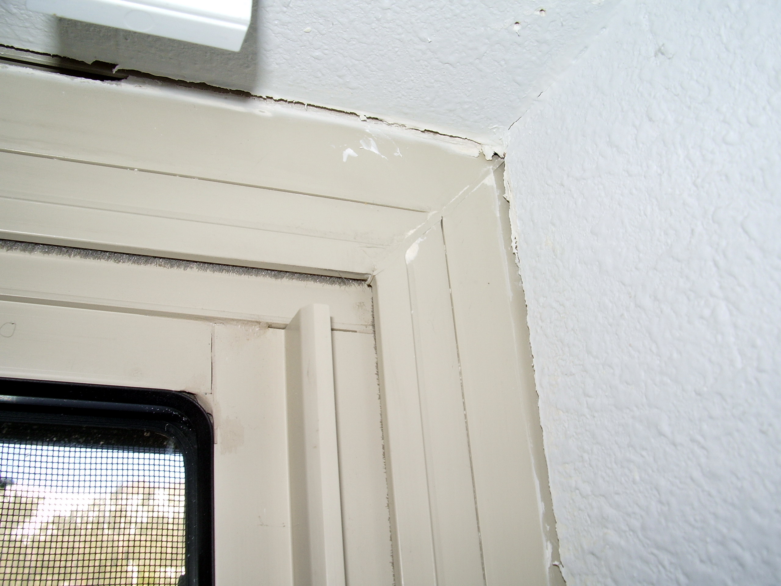 Close-up of cracked and separated caulk along interior window trim where the frame meets the wall.