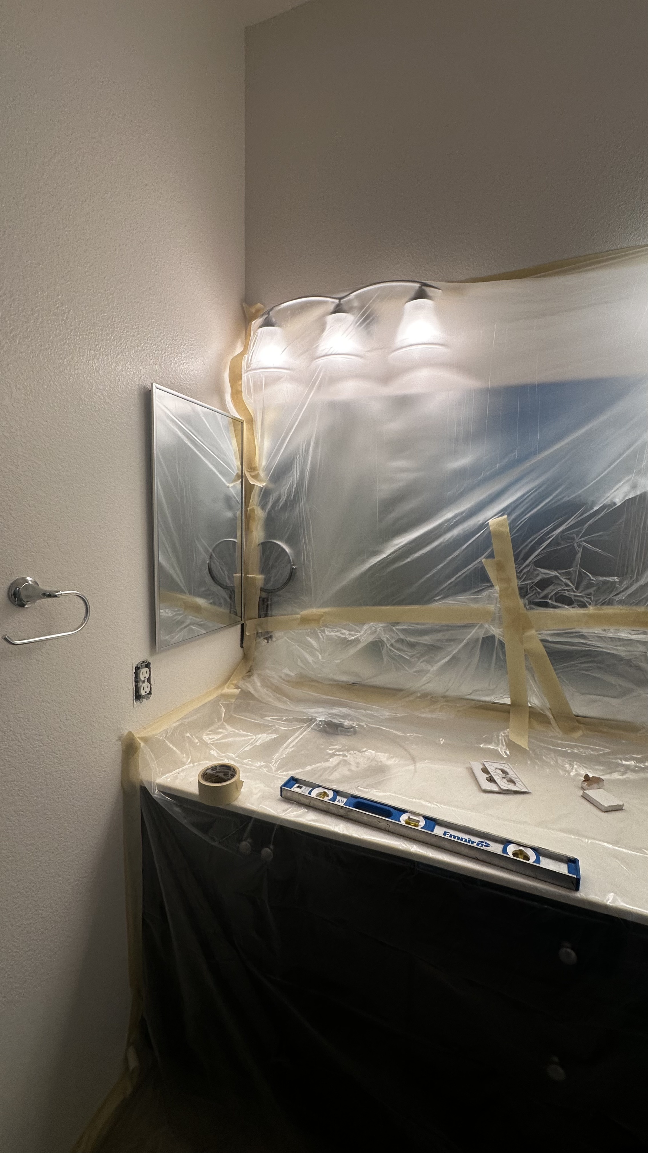 A bathroom vanity and mirror are covered with plastic and tape, showing meticulous preparation for drywall repair or painting in a Las Vegas residence.