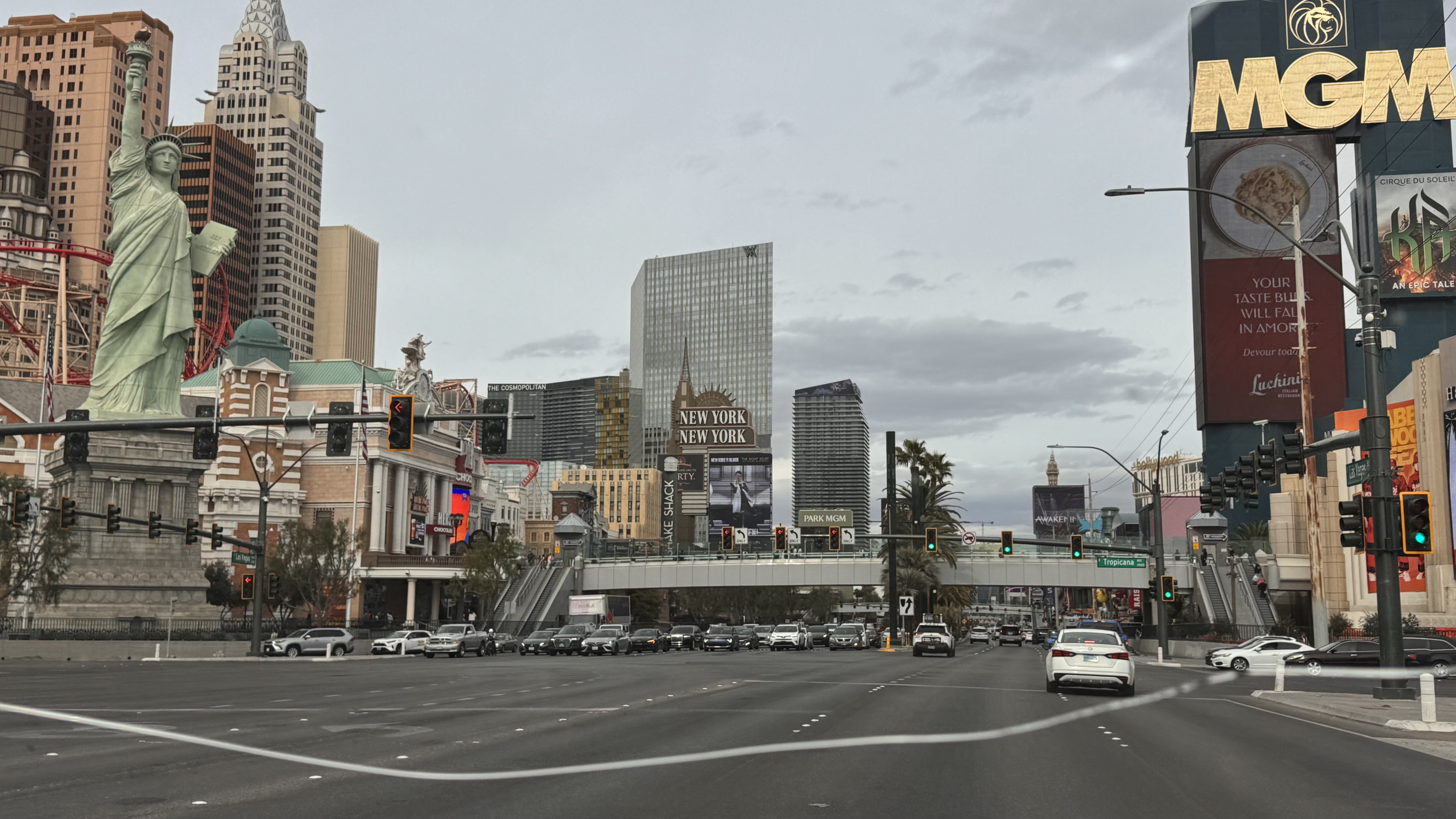 Las Vegas Strip scene showing the replica Statue of Liberty, New York New York hotel, and MGM Grand sign with traffic and city buildings under an overcast sky.