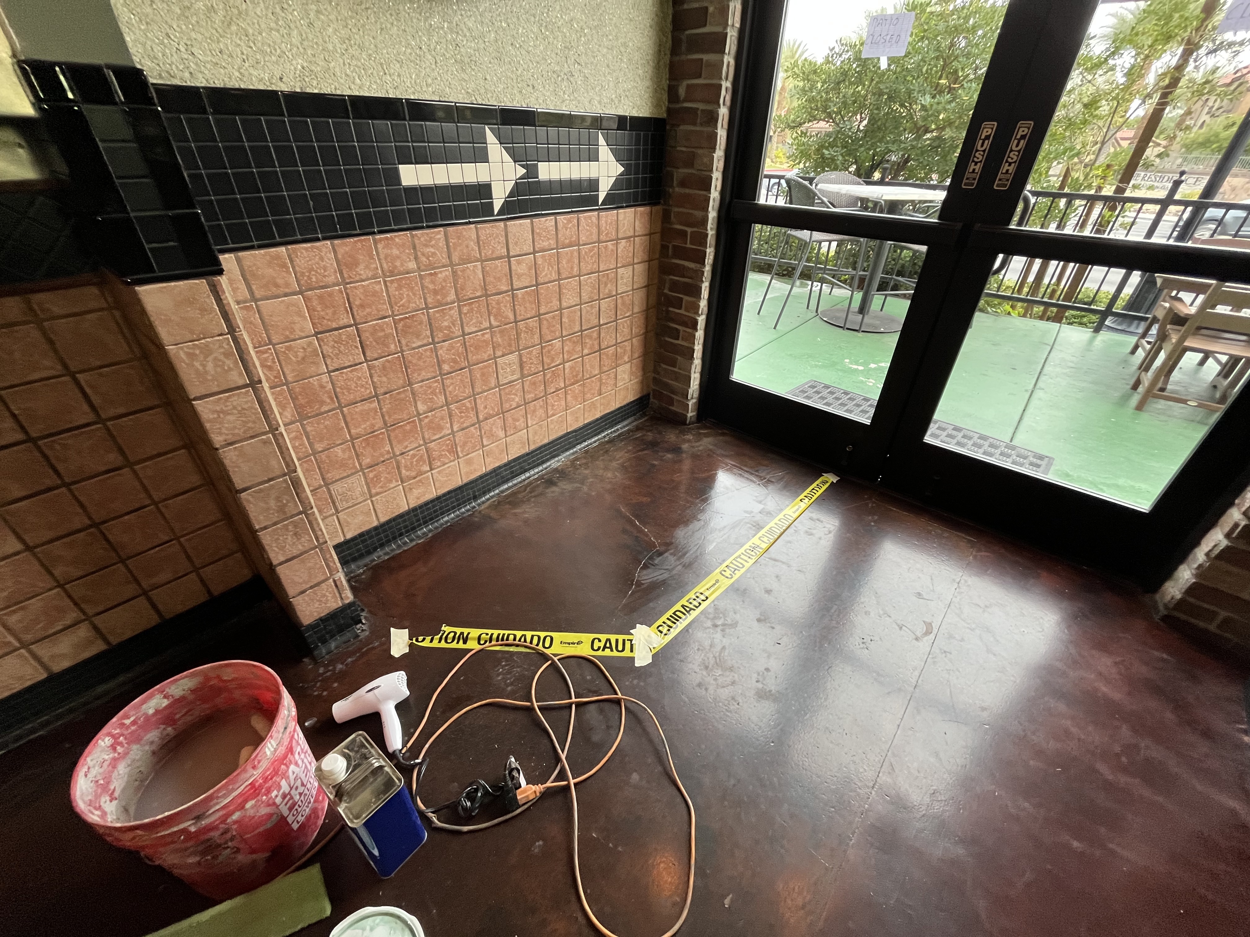 A patio floor refinishing work area with tools and caution tape near glass doors in Las Vegas