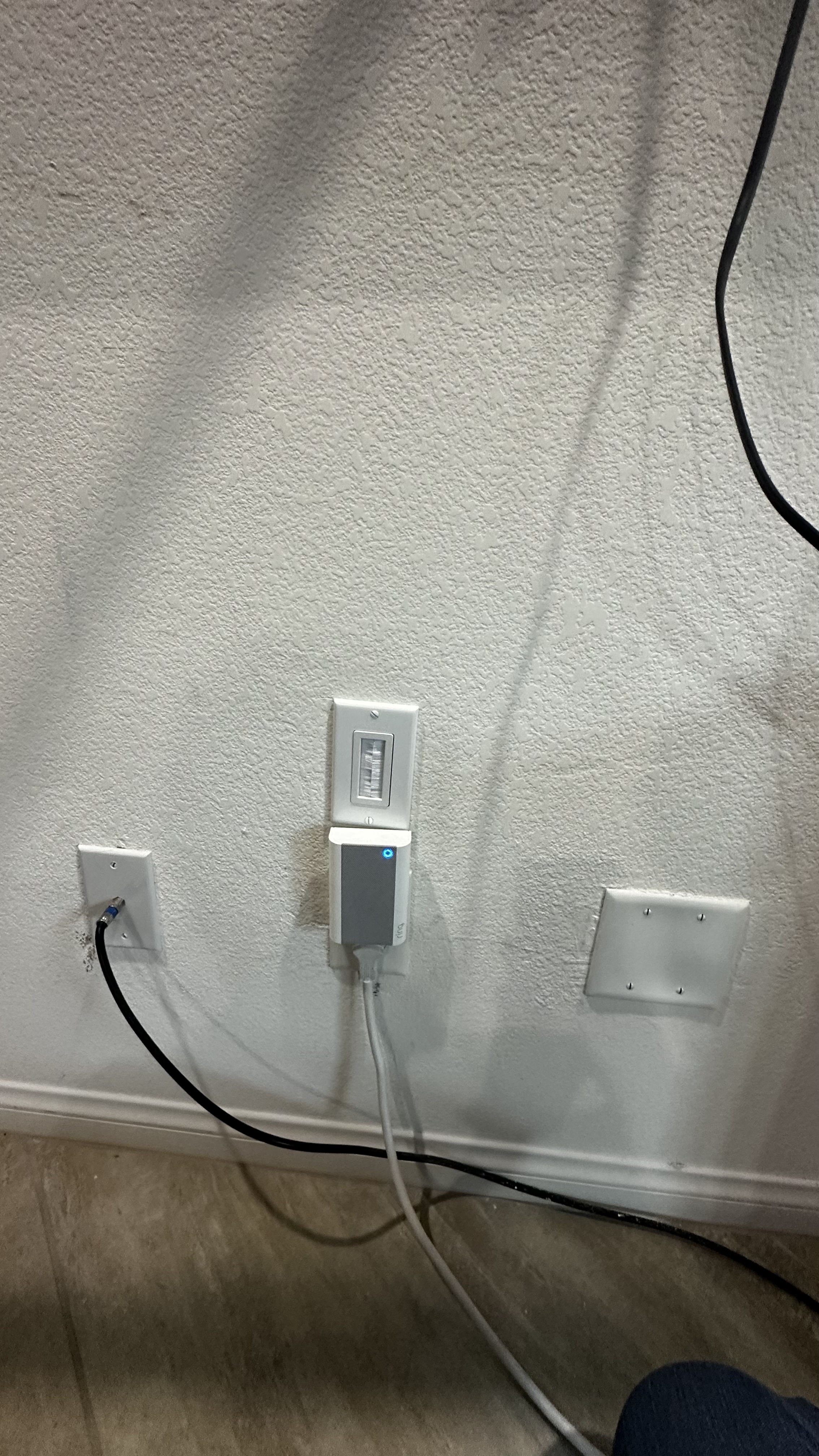 A smart home device with a blue indicator light is plugged into an electrical outlet on a textured white stucco wall, showing proper installation for smart home systems.