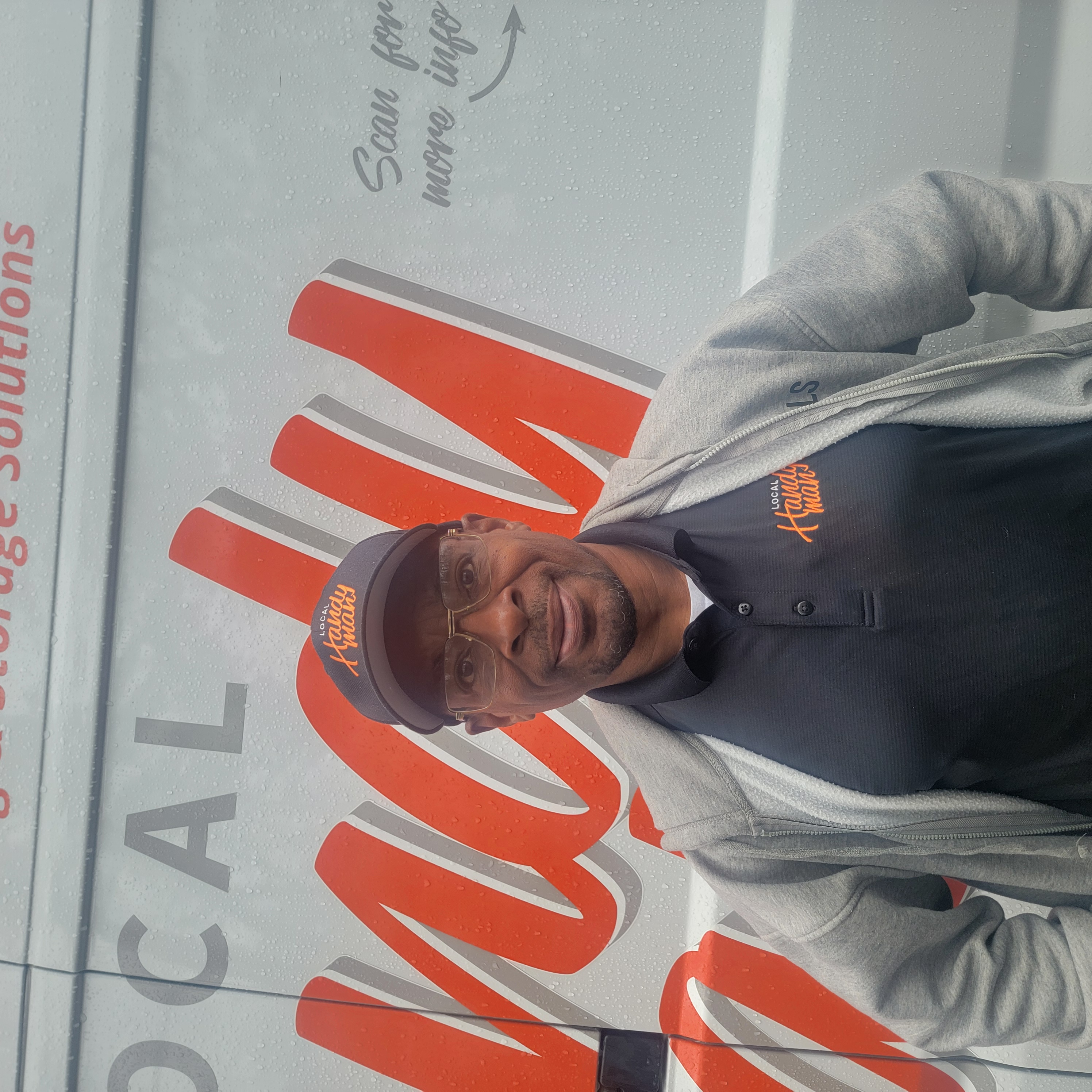 Aaron Brown wearing a Local Handyman cap and polo, standing in front of a company van.