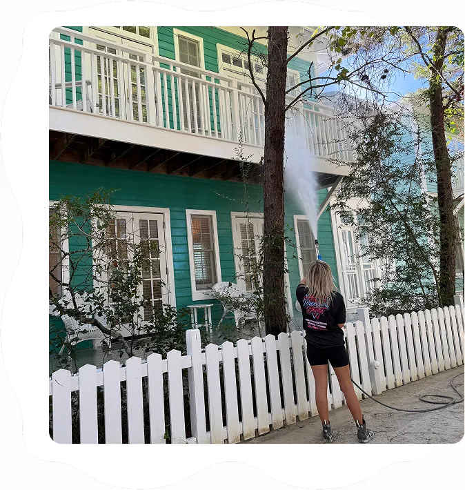Front view of a person pressure washing a green house exterior, targeting the balcony and porch area.