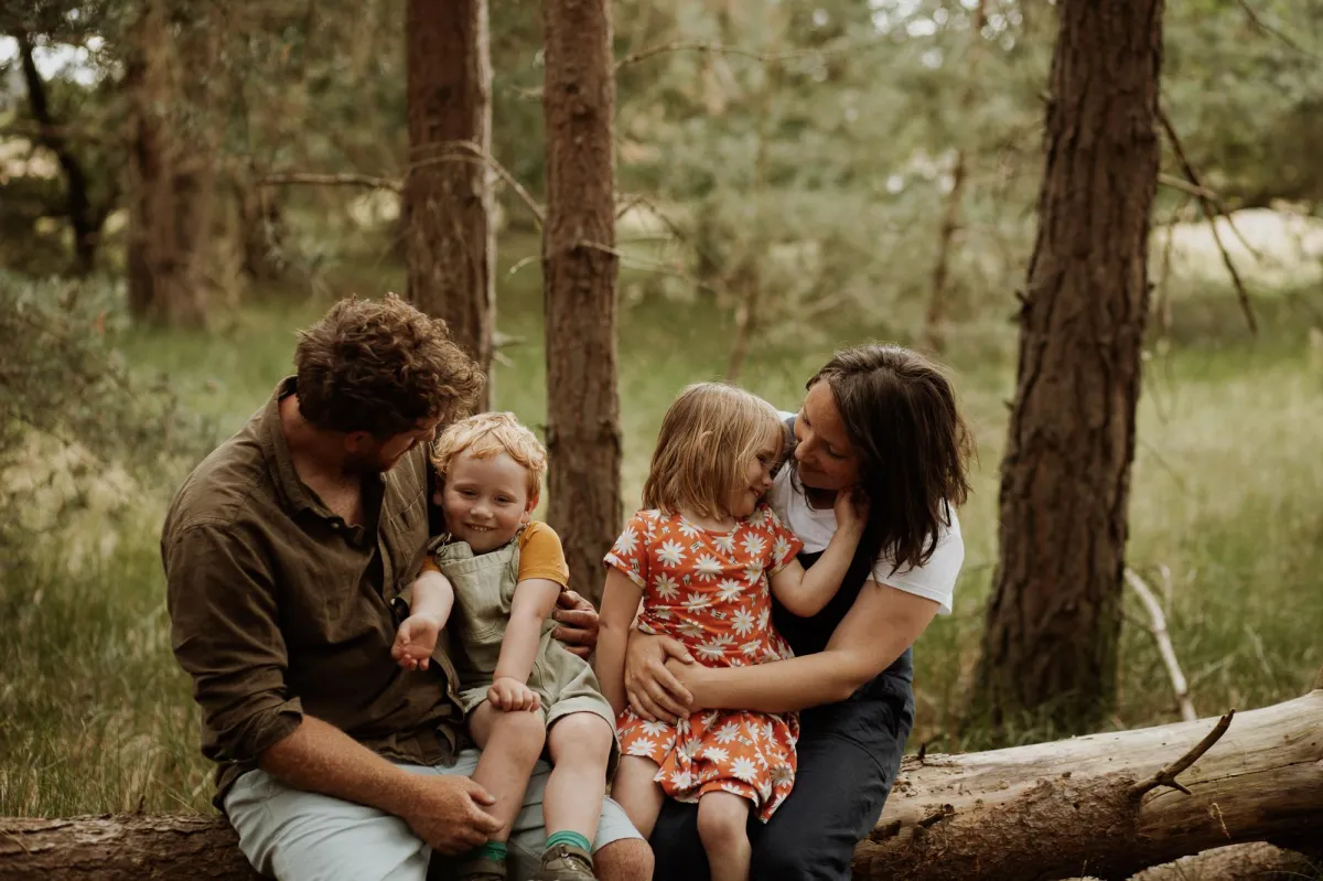 Photography of two parents with a boy and a girl on a log in the forest in Suffolk