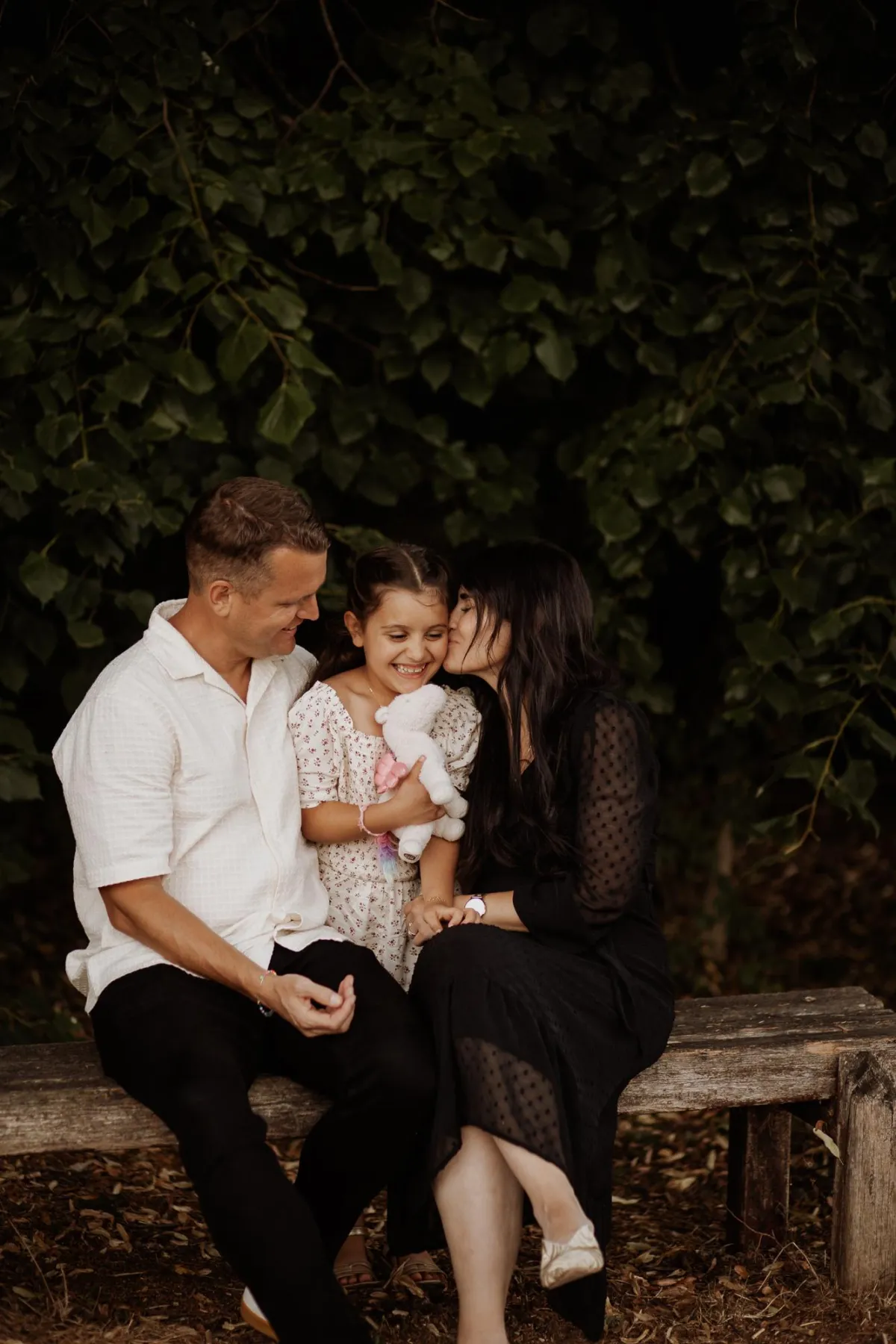 photo of family on a bench giving their daughter a kiss in Nowton Park in suffolk