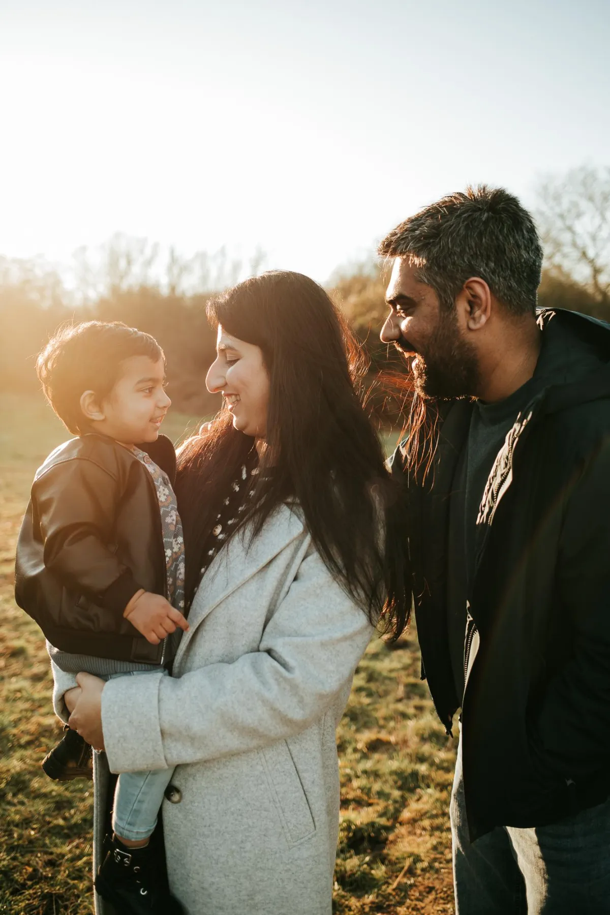 family photographer in suffolk taking photo of parents with their little boy in golden hour