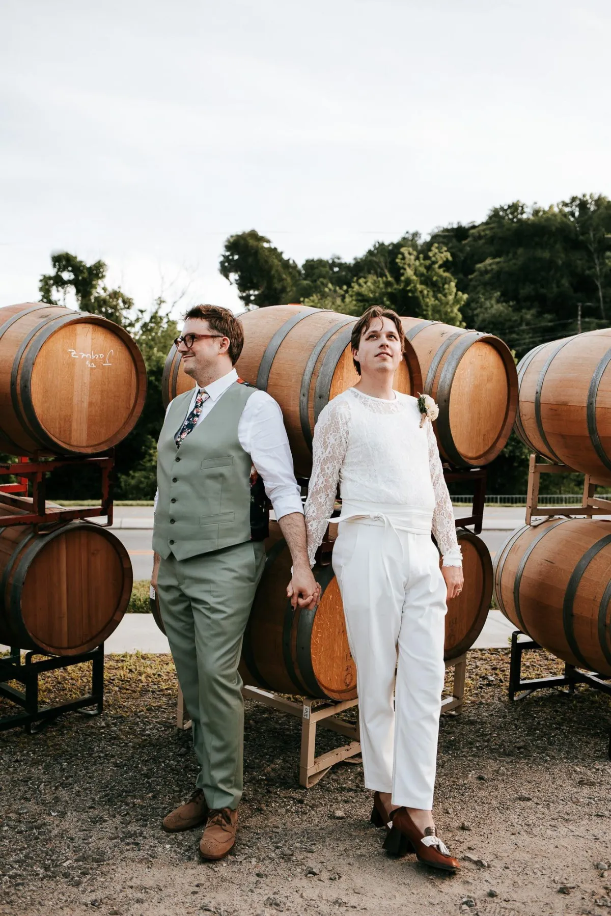 Photo of a gay couple holdng hands in front of win barrels looking in different directions