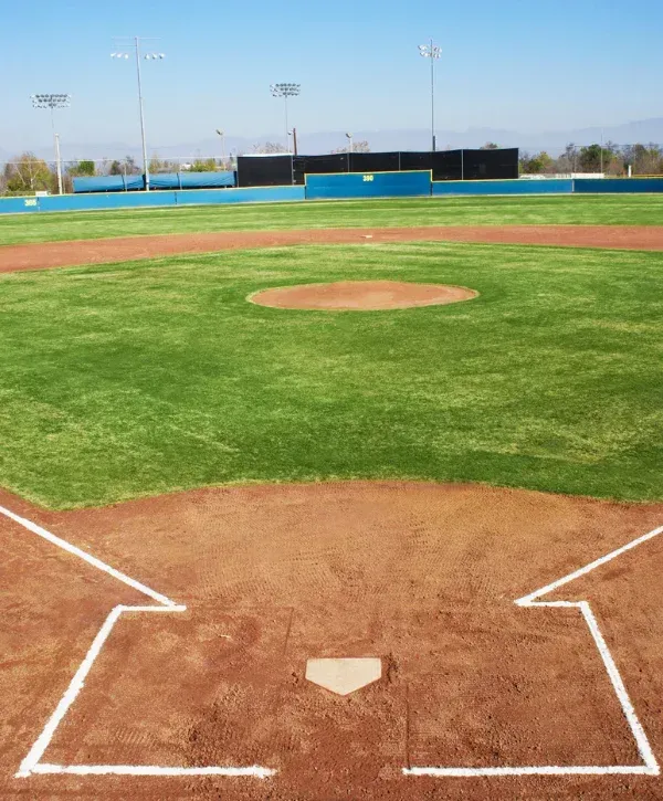 A view from home plate on a brightly lit baseball field, showing the pitcher's mound and outfield in the distance.