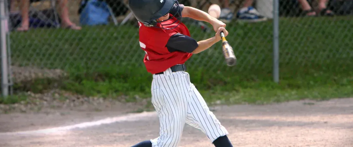 A young boy in a red jersey and pinstripe pants swinging a baseball bat with motion blur.
