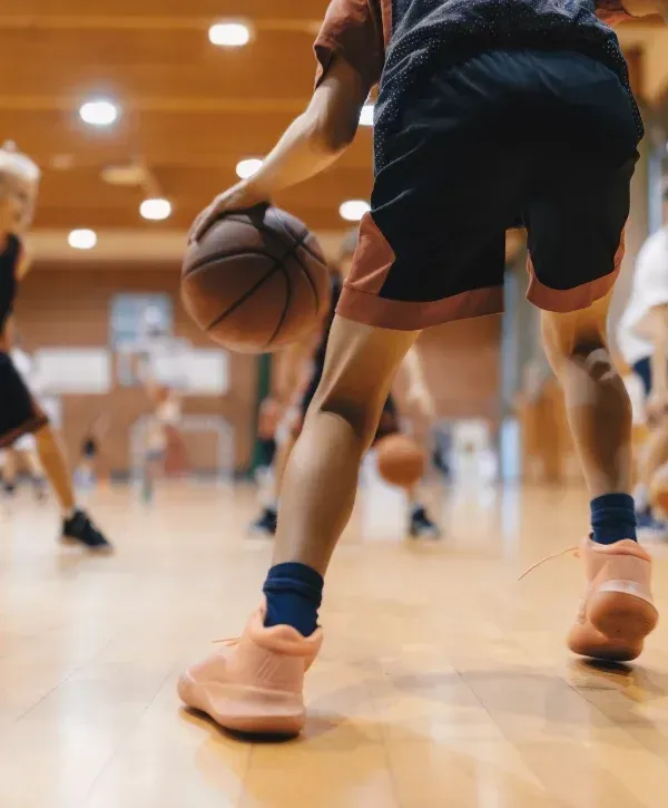 A young basketball player in black and red shorts dribbles the ball on a wooden court during practice.