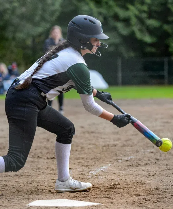 A female softball player wearing a black and gold jersey with number 21 on the back, holding a yellow softball.