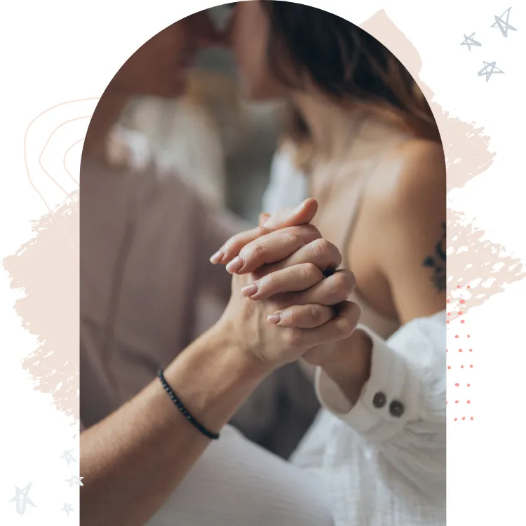 Close-up of a couple holding hands tenderly, emphasizing their connection and intimacy, with soft, blurred background elements.