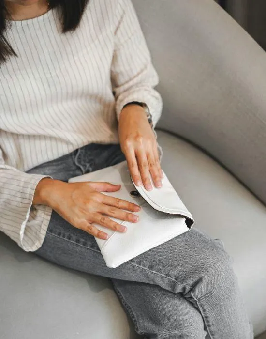 Close-up of a woman sitting on a sofa, holding a white clutch bag, dressed in casual neutral tones, symbolizing minimalism and intentional living.