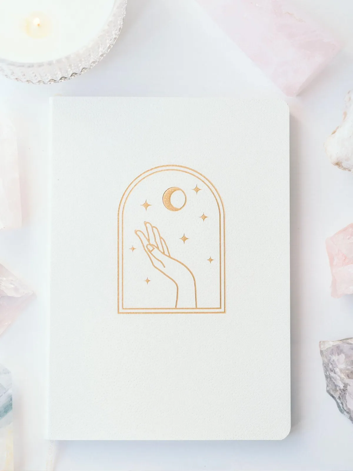 Minimalist journal with a celestial hand and moon design surrounded by crystals and a candle. Ideal for spiritual journaling and manifestation