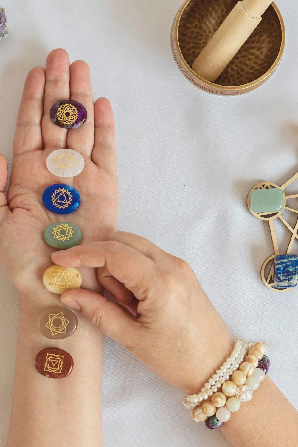 An open hand displaying chakra stones aligned with the body's energy centers, each etched with golden chakra symbols. The serene setup includes healing crystals, a singing bowl, and wooden elements, symbolizing energy balancing and spiritual harmony.