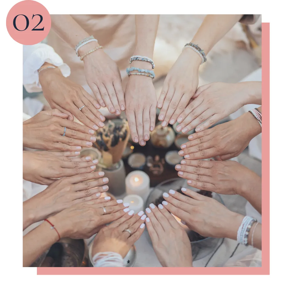 A group of women forming a heart shape with their hands over a table adorned with candles and crystals, symbolizing connection, healing, and empowerment.