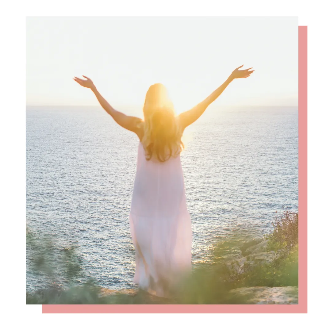 A serene woman in a flowing white dress with arms raised toward the sky, standing on a cliff overlooking the ocean, symbolizing transformation and hope.