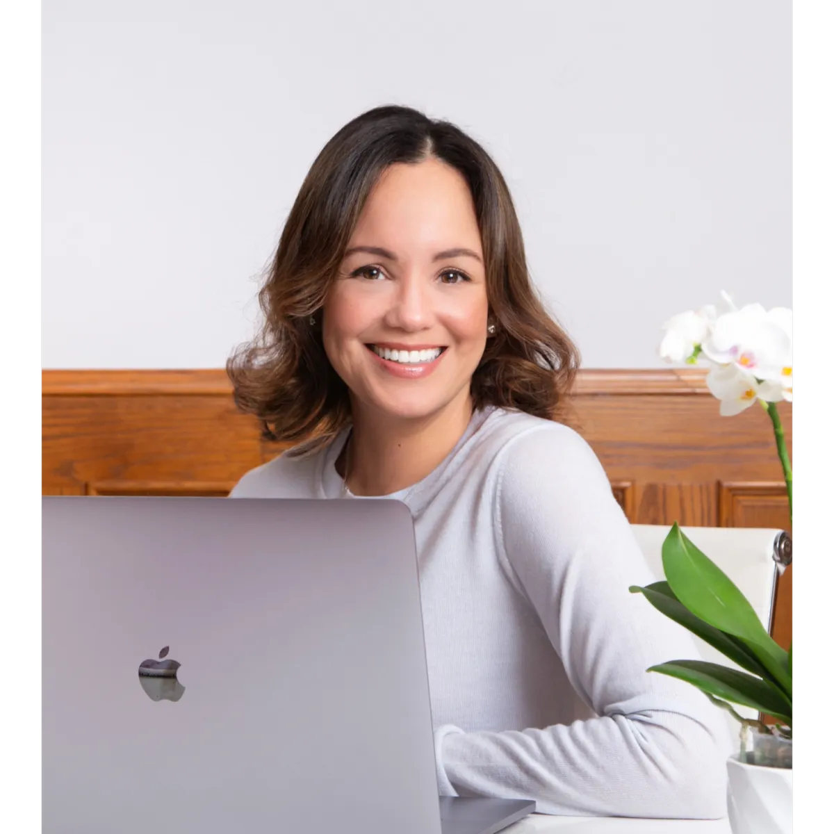 Jeannette, a self-love coach for sober women, smiling confidently while working on a laptop with a calming, minimalist background featuring an orchid.