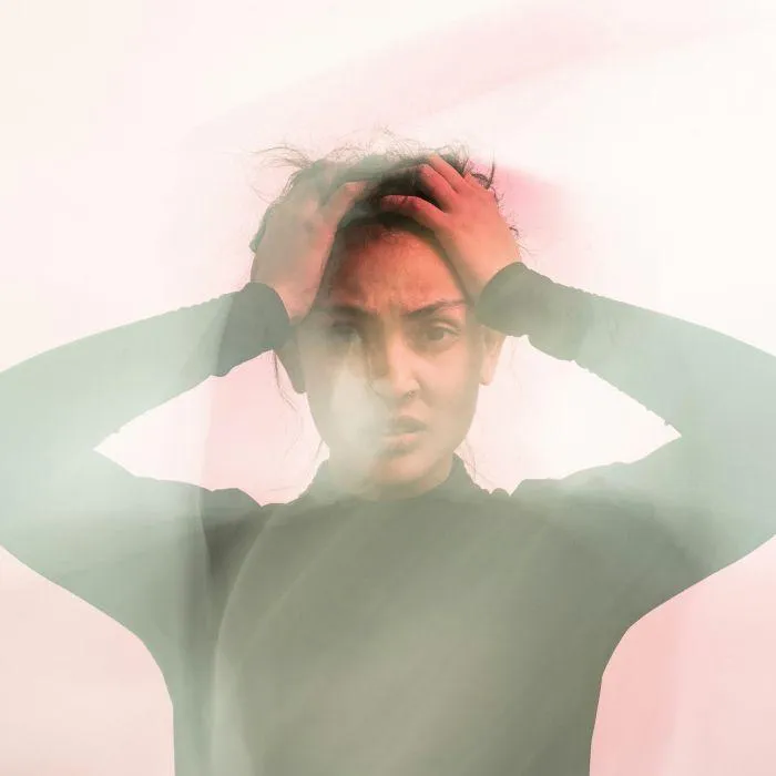 A blurred image of a person with hands on their head, conveying a sense of confusion or overwhelm, with pink and blue light effects around them."