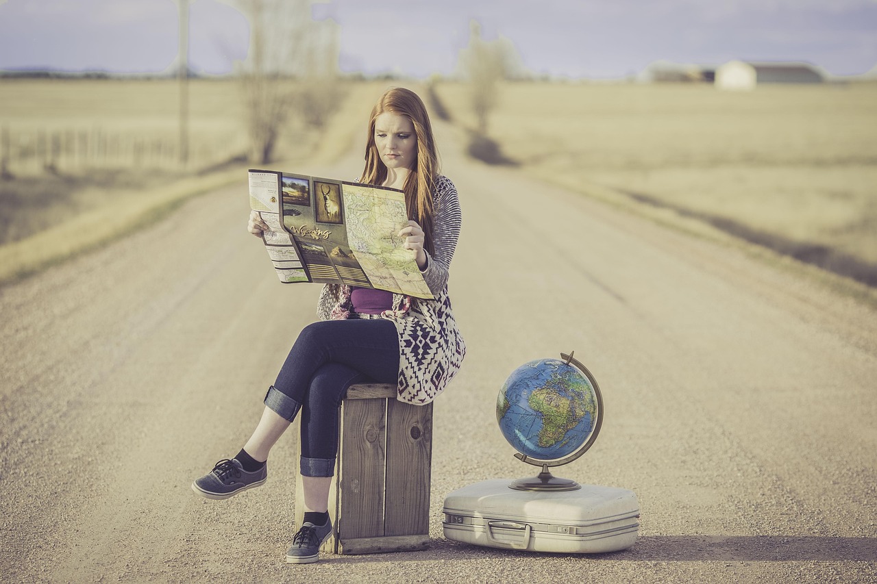 your woman sitting on suitcase with  globe next to her she is sitting on a tarmac