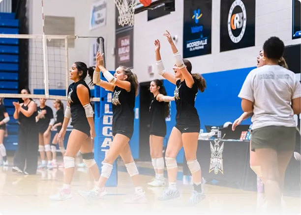 Girls practicing hitting and blocking at the net in a volleyball gym.
