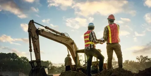 Construction workers supervising an excavator at a job site during sunset for earthworks project management