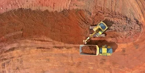 Aerial view of construction vehicles performing earthworks at a red soil excavation site