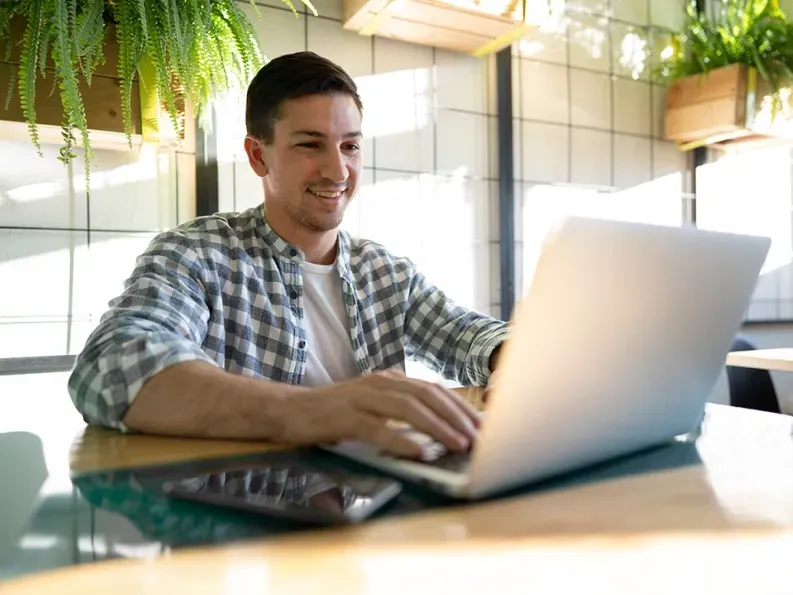 Young professional working on a laptop in a modern office space with natural light and plants