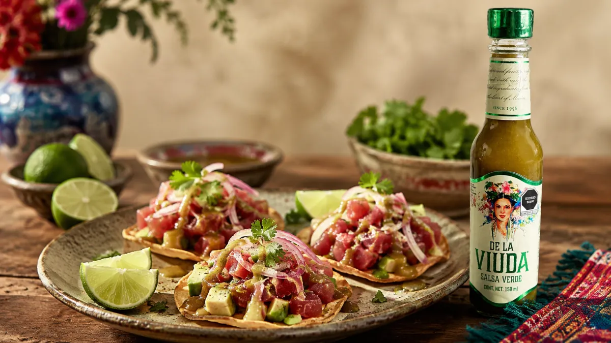 Tostadas de atún fresco con aguacate, pepino, cilantro, limón y salsa verde De La Viuda sobre una mesa mexicana.