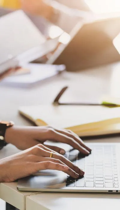 Stock photo of a woman's hands on a laptop sitting on a bed, symbolizing a relaxed approach to starting a strategy session to simplify business tech.