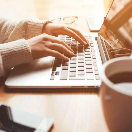 Stock photo of a woman's hands on a laptop sitting on a bed, symbolizing a relaxed approach to starting a strategy session to simplify business tech.